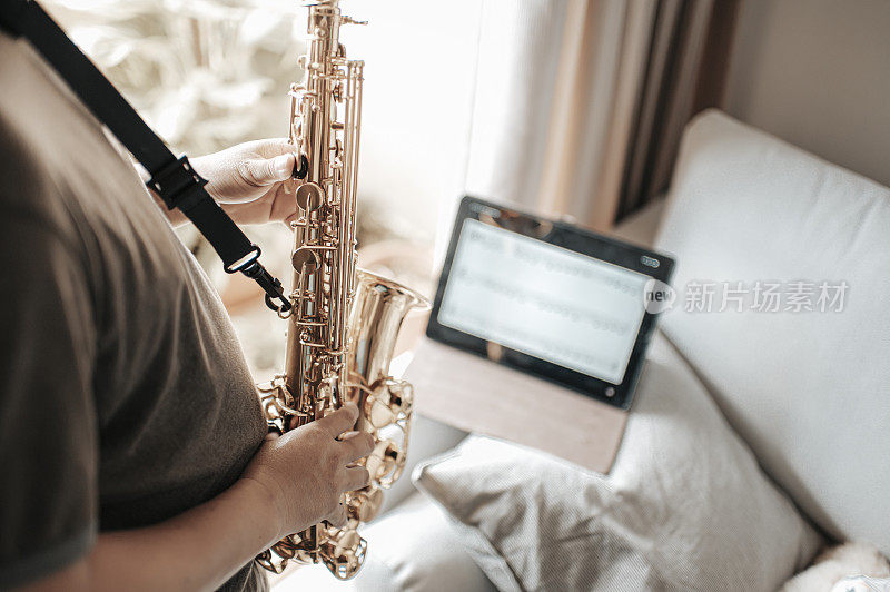 asian chinese mid adult man practicing saxophone  in living room with online class using digital tablet